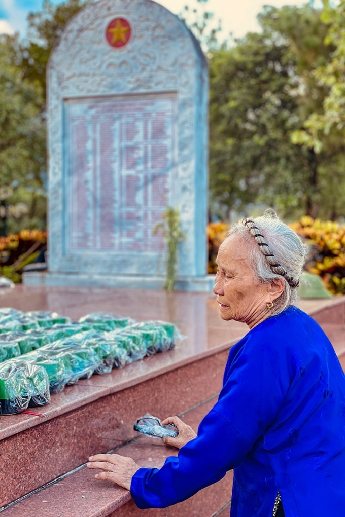  Bà Phạm Thị Hoa xúc động ngồi bên ngôi mộ tập thể là nơi an nghỉ của chồng. (Ảnh: Nguyễn Nga)